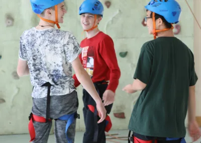3 smiling teenagers in climbing harnesses and helmets