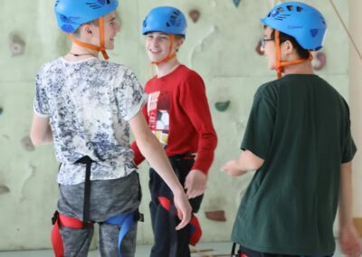 3 smiling teenagers in climbing harnesses and helmets