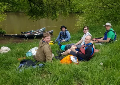 Group on riverbank with canoes in background enjoying a picnic